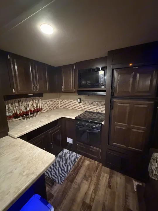 Compact RV rental kitchen featuring dark wood cabinets, light countertops, sink, stove, microwave, and refrigerator.. Forest River Palomino Puma 2018