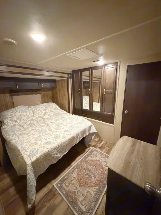 Cozy rv rental bedroom features a bed with a floral comforter, mirrored cabinets, and wood-paneled walls.. Forest River Palomino Puma 2018