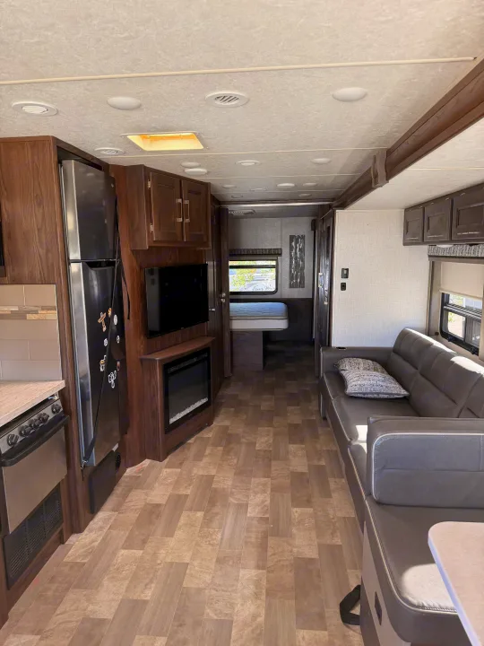Modern RV rental interior showing living area with sofa, TV, fireplace, kitchen, and bedroom access.. Coachmen Mirada 32SS 2019