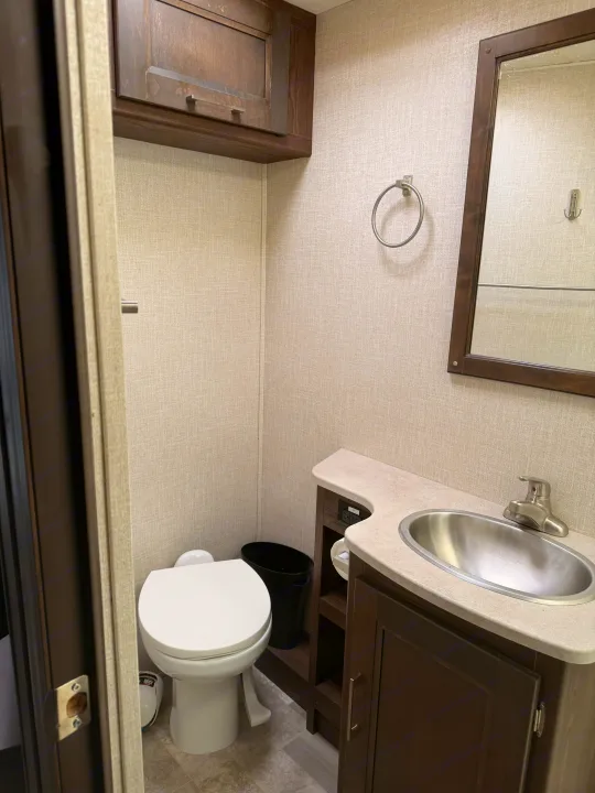 Compact RV rental bathroom featuring a toilet, sink, mirror, and storage cabinet, ideal for travel accommodations.. Coachmen Mirada 32SS 2019