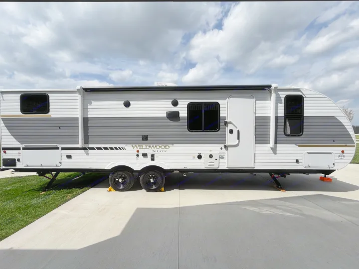 Side view of a white and gray Wildwood X Lite travel trailer RV rental, parked on concrete under a cloudy sky.. Forest River Wildwood X-Lite 273QBXL 2026