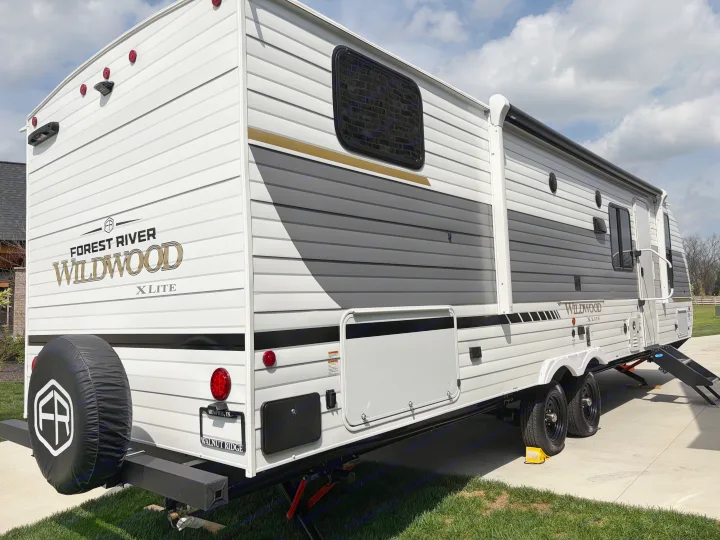Side and rear view of a white Forest River Wildwood X-Lite travel trailer, ideal for an rv rental adventure, parked on pavement.. Forest River Wildwood X-Lite 273QBXL 2026