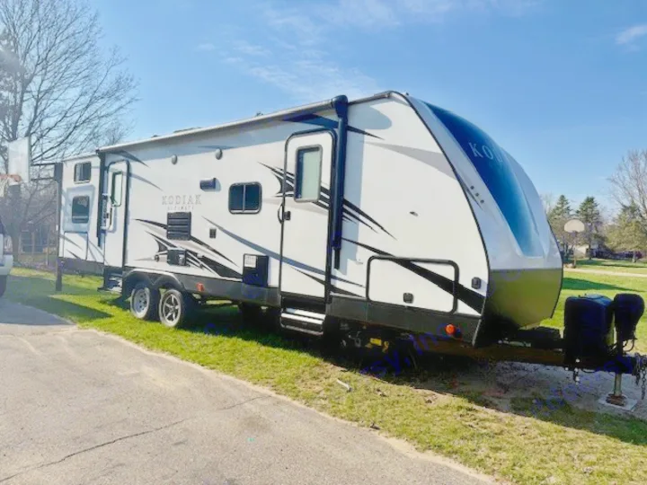 A white Kodiak Ultimate travel trailer, ideal for your next RV rental or camping adventure. Parked outdoors with its awning extended.. Kodiak Ultimate 288BHSL 2018