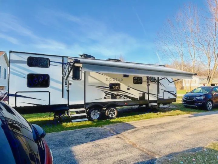 A white Kodiak Cub RV rental travel trailer is parked with its awning extended on a sunny day.. Kodiak Ultimate 288BHSL 2018