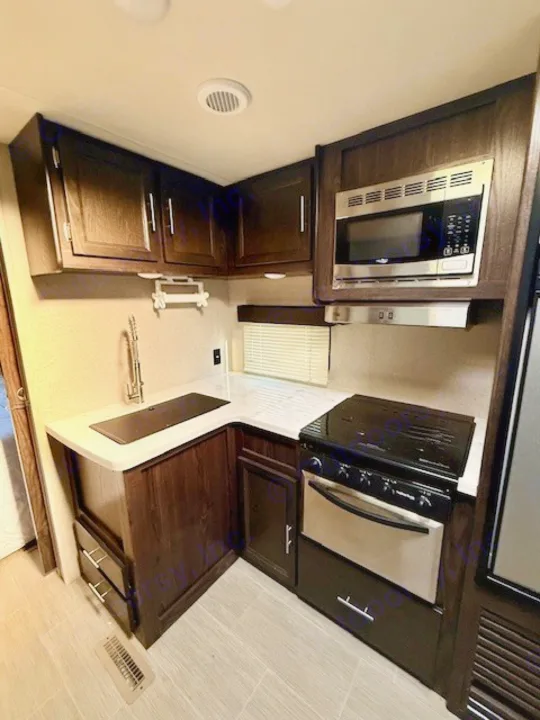 Clean RV rental kitchen: dark wood cabinets, modern appliances (sink, stove, microwave), light countertop & floor for your travels.. Kodiak Ultimate 288BHSL 2018