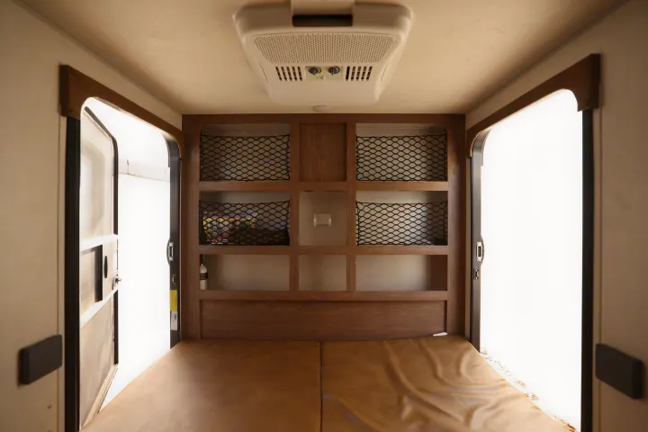 RV rental interior: bed, ceiling AC, open doors, and wooden storage with cargo nets for travel essentials.. No Boundaries 10 2020
