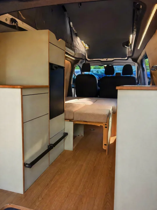 RV rental: Campervan interior features a convertible bed, storage cabinets, built-in fridge, and front seats.. Ford Custom 2024