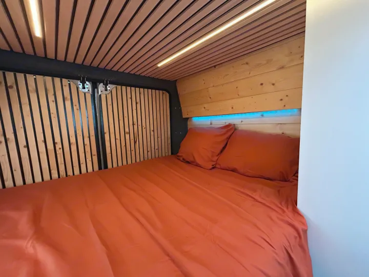 Cozy RV rental bed featuring warm wood paneling, ambient ceiling light, and blue LED accents above the headboard.. FIAT Ducato 2013