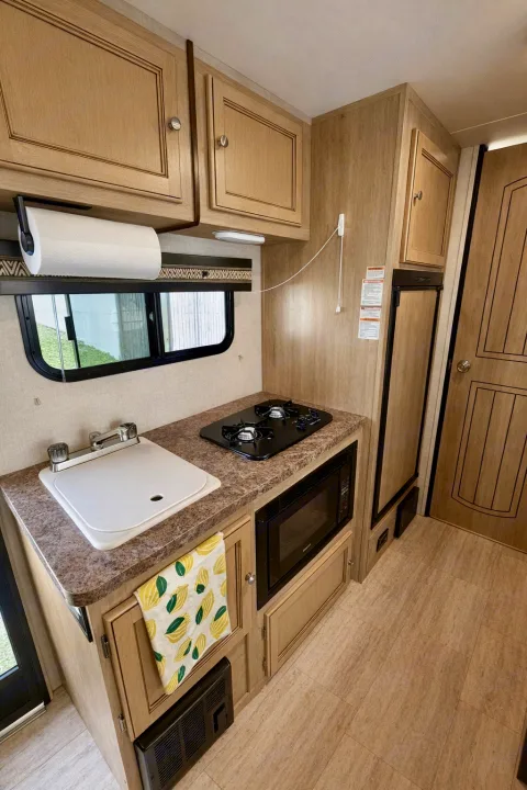 Compact RV rental kitchen featuring a sink, stove, microwave, and refrigerator in light wood cabinetry. Bright interior view.. Palomino Real Lite Mini 2017
