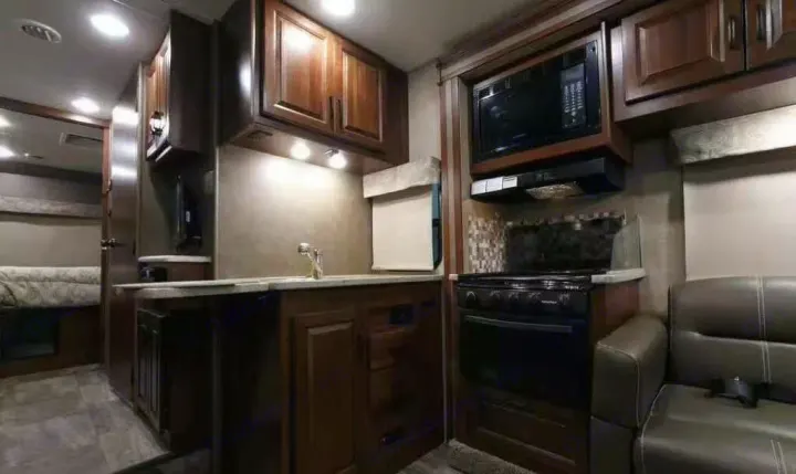 Spacious RV rental interior. Features a full kitchen with dark cabinets, microwave, stovetop, sink, and comfortable seating.. Forest River forester 2017