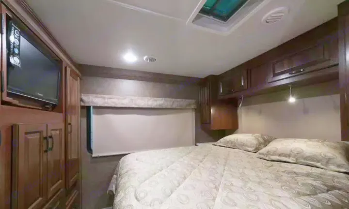 This cozy RV rental bedroom features a comfortable bed with patterned bedding, a wall-mounted TV, and ample storage cabinets.. Forest River forester 2017