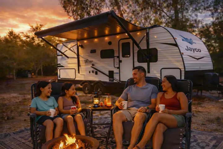 A family relaxes by a warm campfire beside their RV rental at sunset. Cherished family camping memories.. jayco 235MBH Jay Flight TT 2025