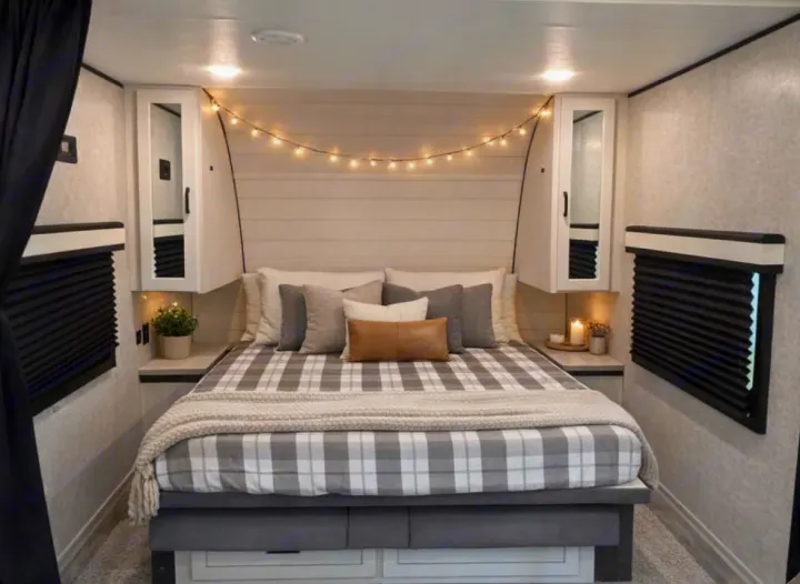 This cozy RV rental bedroom features a plaid bed, soft pillows, fairy lights, and convenient storage, ideal for your next trip.. jayco 235MBH Jay Flight TT 2025
