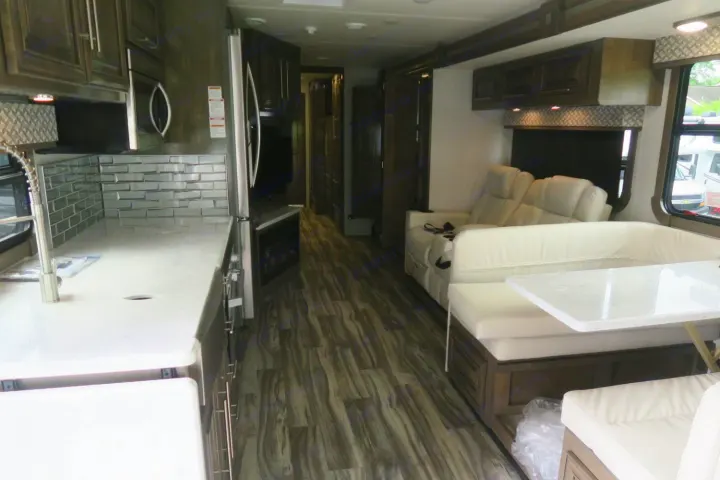 Inside this rv rental: sleek kitchen with backsplash, white dining booth & recliners, dark wood cabinets, and wood-look flooring.. Forest River Georgetown 2020