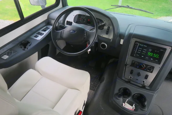 Detailed view of an RV rental's modern cockpit. Features a Ford steering wheel, dashboard controls, and a digital radio display.. Forest River Georgetown 2020