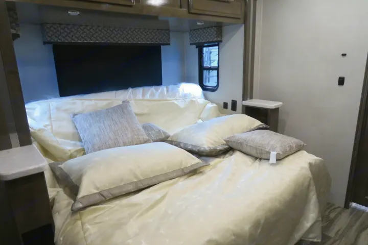 Modern RV rental bedroom with a neatly made bed, cream bedding, various pillows, and overhead cabinets. Ready for your travels.. Forest River Georgetown 2020