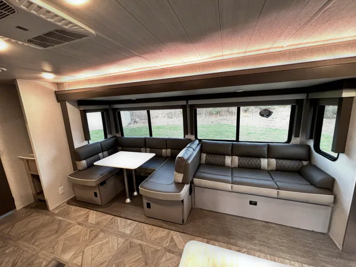 Modern RV rental interior with a comfortable U-shaped dinette, stylish gray seating, and bright windows.. Forest River Wildwood 2024