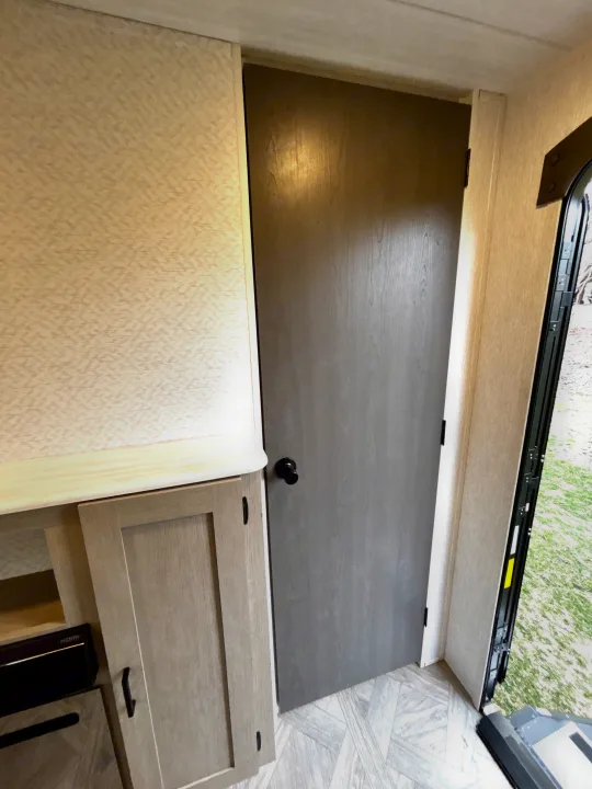 RV rental interior featuring a gray door, light wood cabinets, patterned walls & floor, and an open entrance.. Forest River Wildwood 2024