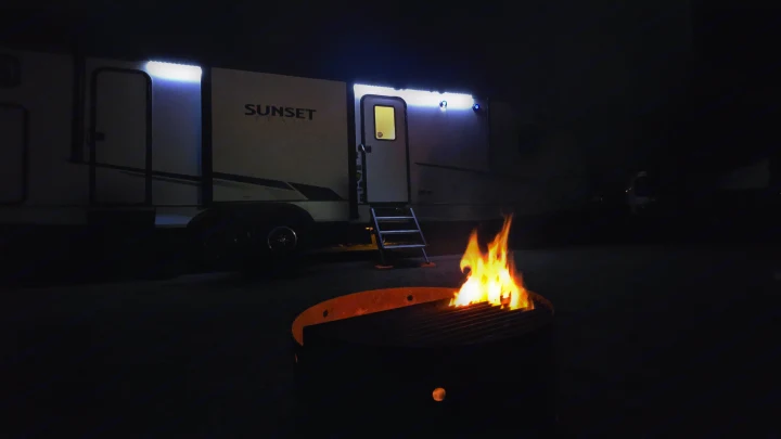 An rv rental glows under awning lights next to a roaring campfire in a fire pit at night.. Crossroads RV Sunset Trail 2022