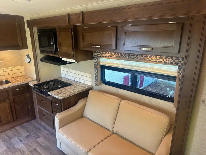 RV rental interior: modern kitchen with microwave, stove, and sink. Features wood cabinets, light backsplash, and a comfortable sofa.. Jayco Redhawk 2019