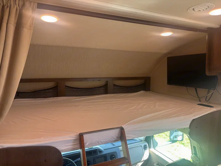 This RV rental's over-cab bunk bed offers a cozy sleeping area with mesh storage, a TV, and recessed lighting.. Jayco Redhawk 2019