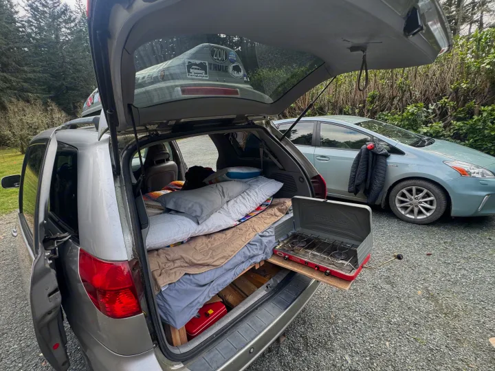 Creative car camping setup. See inside this RV rental alternative with a bed & camp stove pulled from the open tailgate.. Toyota Sienna Limited XLE Camper Van 2004