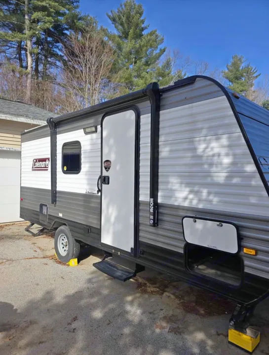 Gray & white Coleman travel trailer, ideal for rv rental, parked outdoors. Features an awning, door, and storage.. Dutchmen Coleman Lantern LT 2022