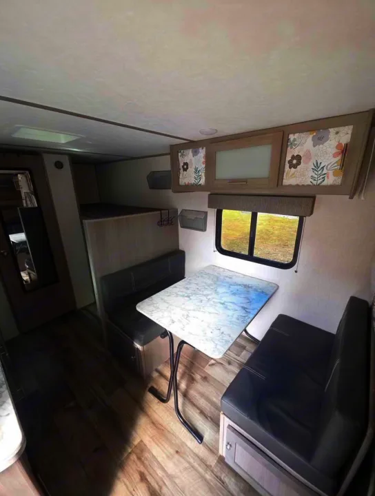 Inside an rv rental: dinette with dark booth seating, white table, bunk beds, floral cabinets, and wood-look floor. Bright interior for travel.. Dutchmen Coleman Lantern LT 2022