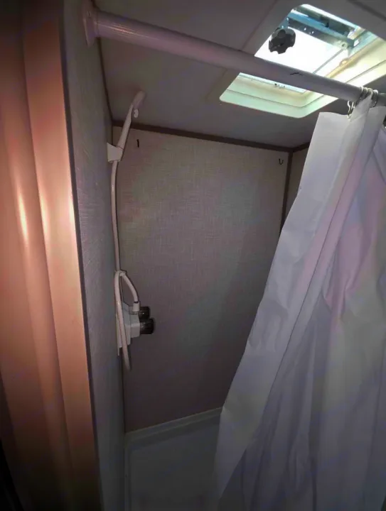 Compact RV rental shower stall with a handheld showerhead, water controls, and a ceiling skylight/vent.. Dutchmen Coleman Lantern LT 2022
