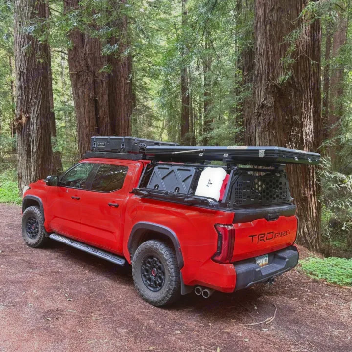This custom red adventure truck, equipped with a rooftop tent, is ready for rv rental in a scenic redwood forest.. Toyota Landcruiser 2022