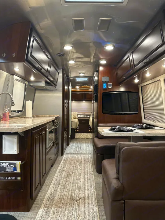 This upscale rv rental showcases a modern interior with a fully equipped kitchen, dining booth, and a view to the cozy rear bedroom.. Airstream Classic 2017