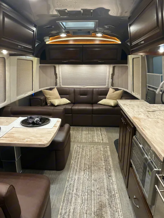 Spacious RV rental interior: dark leather sofa, modern kitchen with microwave, dining table, and sleek wood cabinetry.. Airstream Classic 2017