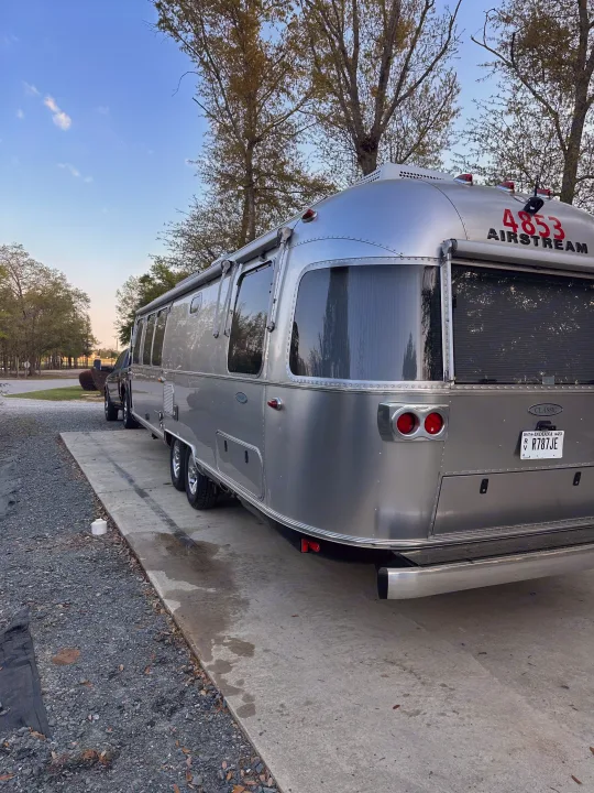 A classic silver Airstream rv rental (travel trailer) is seen parked on a concrete pad at a campsite, with a truck nearby.. Airstream Classic 2017