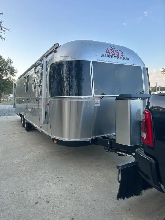 This iconic silver Airstream travel trailer, perfect for an RV rental, is hitched to a black pickup truck on concrete.. Airstream Classic 2017