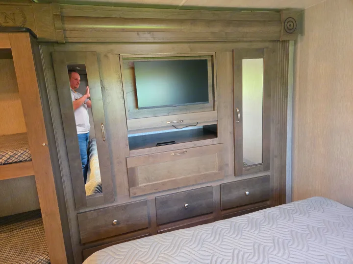 RV rental bedroom with built-in entertainment unit, ample storage, and bed. Mirrored wardrobes are visible.. Nexus RV Phantom 2024