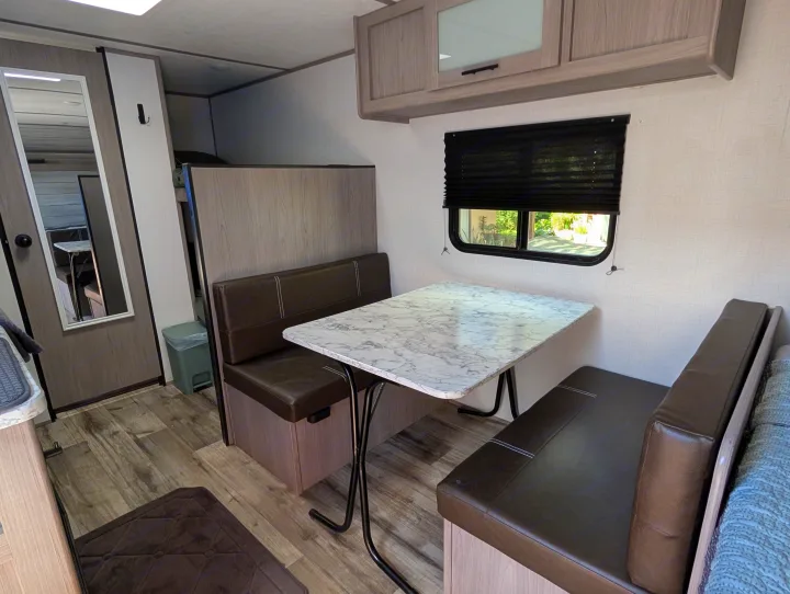 RV rental dinette area featuring a modern, light marble-patterned table, dark brown bench seats, and wood-look cabinets.. Dutchmen Coleman Lantern LT 2023