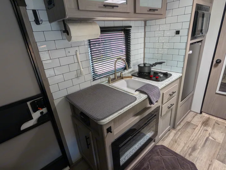 Modern RV rental kitchen interior featuring a sink, stovetop, microwave, and electric fireplace with stylish details.. Dutchmen Coleman Lantern LT 2023