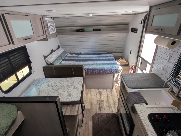 Cozy RV rental interior showcasing a bed, dinette with a faux marble table, and a compact kitchen area.. Dutchmen Coleman Lantern LT 2023