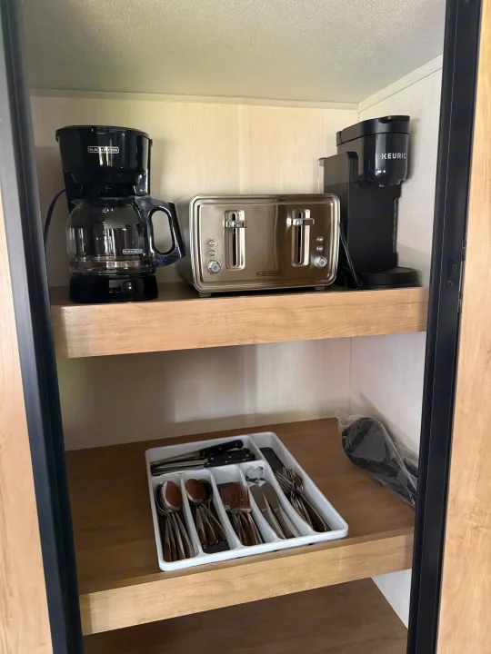 RV rental kitchenette: Black+Decker coffee maker, toaster, Keurig, and cutlery neatly arranged on wood shelves.. Forest River Grey wolf 2026