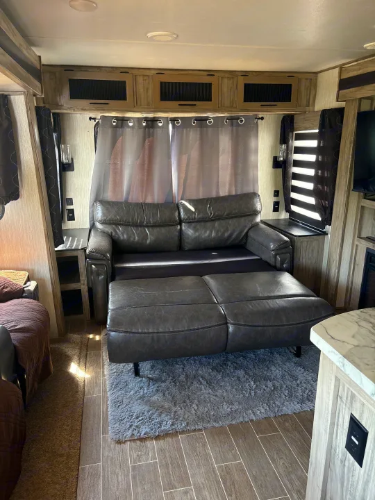 Rv rental interior: dark gray leather sofa bed extends over a fluffy rug, surrounded by light wood cabinetry.. Forest River Cherokee Alpha Wolf 2021