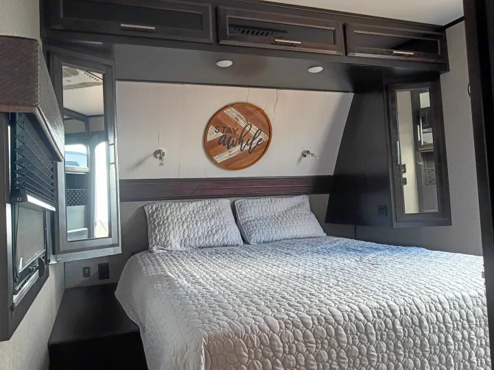 This RV rental offers a comfortable bedroom with a queen bed, decorative 'STAY awhile' sign, and convenient storage.. Jayco Eagle HT 2020