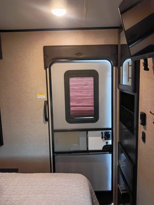 RV rental interior: A bedroom with a main door, window blind, bed, wall-mounted TV, and storage shelves.. Jayco Eagle HT 2020