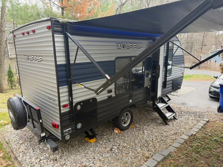 This light gray and blue Wolf Pup travel trailer, an ideal RV rental, has its awning extended with cool blue LED lights.. Forest River Cherokee Wolf Pup 2021