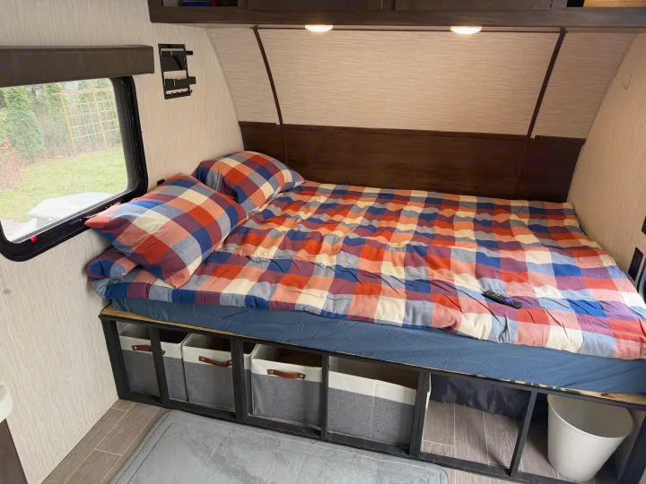 Cozy RV rental bedroom features colorful plaid bedding, a window with outdoor view, and under-bed storage baskets.. Forest River Cherokee Wolf Pup 2021