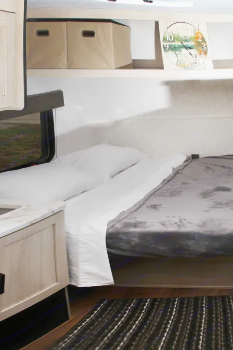 Cozy RV rental bedroom featuring a bed with white linens & gray blanket, built-in storage, and a scenic wall clock.. Palomino Puma Camping Edition 122BHCE 2026