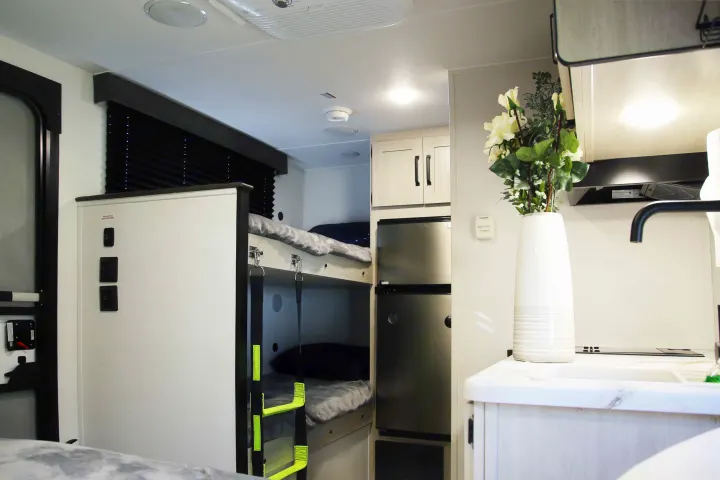 RV rental interior: Compact bunk beds, stainless fridge, and bright kitchen with a sink and floral decor. Ready for travel.. Palomino Puma Camping Edition 122BHCE 2026