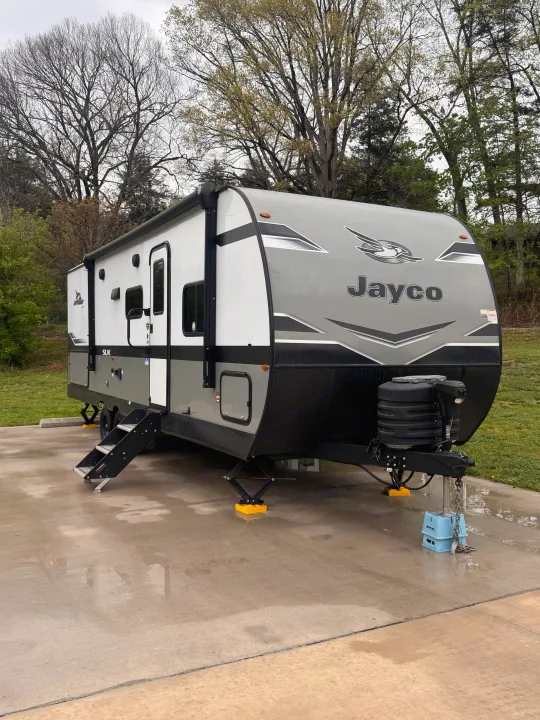 Modern gray & white Jayco travel trailer (RV rental) set up on a damp concrete pad, ready for camping.. Jayco Jay Flight SLX 2024