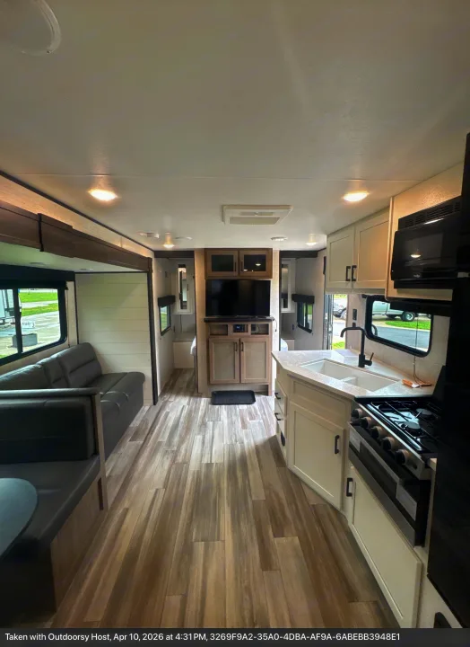 Modern rv rental interior: A bright kitchen with white cabinets, dark sofa, and dinette with wood-look flooring visible.. Jayco Jay Flight SLX 2024