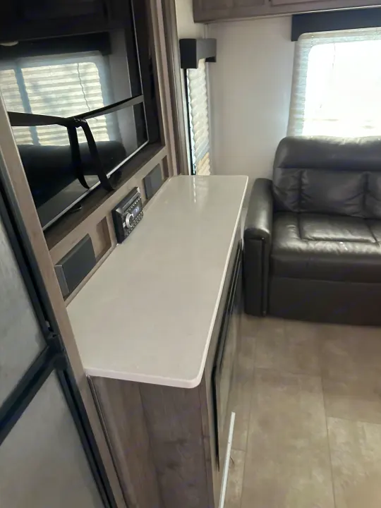 RV rental living space featuring a secured TV, embedded audio system, white countertop, and leather sofa.. Coachmen Apex 2021