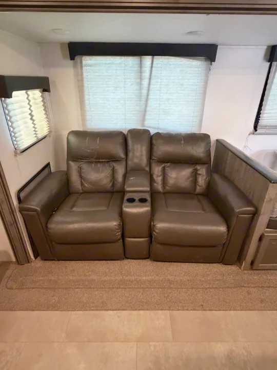 RV rental living space featuring dual brown recliners with a shared console and cupholders, offering cozy seating.. Coachmen Apex 2021